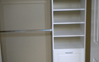 Left Side Reach-in closet with tower of hamper, adjustable shelving and section of double hanging designed for access to storage area. White color. Raised panel finish